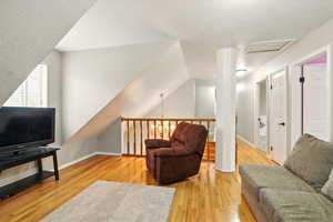 Living room with light wood finished floors, attic access, a textured ceiling, and vaulted ceiling