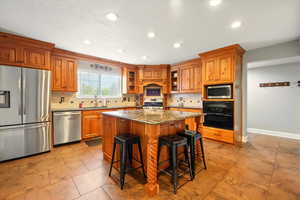Kitchen with dark stone counters, appliances with stainless steel finishes, a breakfast bar area, brown cabinets, and a kitchen island