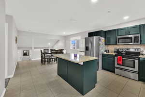 Kitchen featuring green cabinets, stainless steel appliances, light tile patterned floors, a center island, and recessed lighting