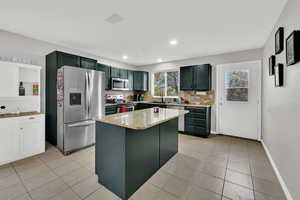Kitchen with tasteful backsplash, stainless steel appliances, a kitchen island, light stone countertops, and light tile patterned flooring
