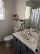 Full bath with vanity, a shower with curtain, dark tile patterned flooring, and healthy amount of natural light