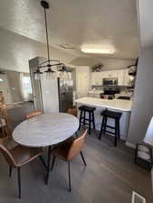 Dining area featuring vaulted ceiling, a textured ceiling, and dark wood-style floors