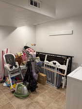 Bedroom featuring a textured ceiling, washer / clothes dryer, light tile patterned flooring, and a nursery area