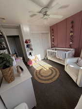 Carpeted bedroom with a nursery area, ceiling fan, a closet, and attic access