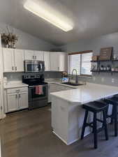 Kitchen featuring a peninsula, stainless steel appliances, a breakfast bar area, white cabinetry, and light countertops
