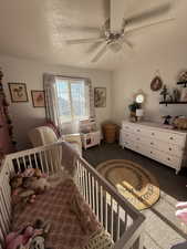 Bedroom featuring carpet floors, a textured ceiling, ceiling fan, and a crib