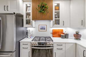 Kitchen featuring stainless steel appliances, white cabinetry, light stone counters, and glass insert cabinets