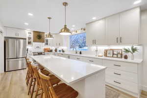 Kitchen with appliances with stainless steel finishes, a kitchen bar, recessed lighting, white cabinets, and decorative light fixtures