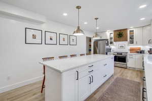 Kitchen with a kitchen bar, white cabinets, appliances with stainless steel finishes, hanging light fixtures, and light wood finished floors
