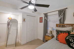 Bedroom featuring a closet, a wainscoted wall, light colored carpet, and a ceiling fan