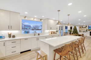 Kitchen featuring open floor plan, light wood finished floors, a kitchen bar, pendant lighting, and a fireplace