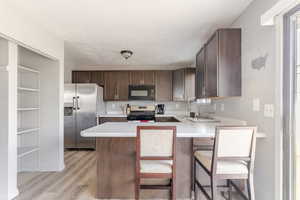 Kitchen featuring dark brown cabinets, light countertops, black appliances, a kitchen bar, and light wood-style floors