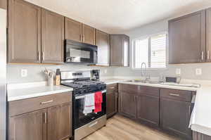 Kitchen featuring stainless steel gas range, black microwave, light countertops, a textured ceiling, and dark brown cabinetry