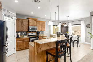 Kitchen featuring brown cabinetry, appliances with stainless steel finishes, pendant lighting, an island with sink, and recessed lighting