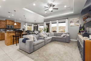 Living room with a tray ceiling, ceiling fan, recessed lighting, and light tile patterned floors