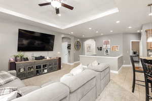 Living area with arched walkways, a raised ceiling, light tile patterned floors, recessed lighting, and ceiling fan