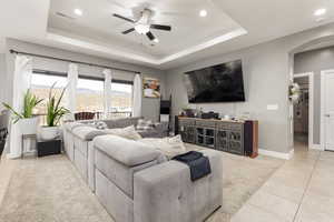 Living area with light tile patterned flooring, arched walkways, a raised ceiling, recessed lighting, and a ceiling fan