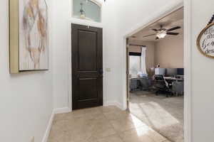 Foyer with light tile patterned flooring, light carpet, and a ceiling fan