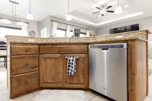 Kitchen featuring hanging light fixtures, brown cabinets, dishwasher, a raised ceiling, and ceiling fan