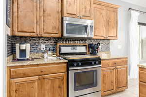 Kitchen featuring stainless steel appliances, light stone countertops, tasteful backsplash, and light tile patterned floors