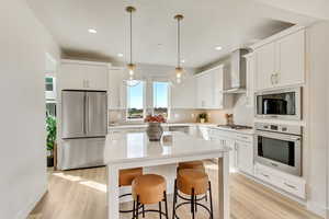 Kitchen featuring appliances with stainless steel finishes, decorative light fixtures, a center island, white cabinetry, and a kitchen bar