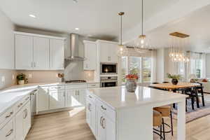Kitchen featuring a center island, white cabinets, hanging light fixtures, tasteful backsplash, and wall chimney range hood