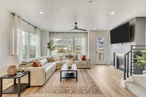 Living room featuring light wood-style flooring, a glass covered fireplace, ceiling fan, stairway, and recessed lighting