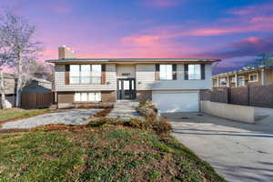 Split foyer home featuring brick siding, a chimney, driveway, and a garage