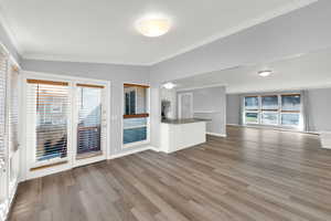 Unfurnished living room featuring crown molding, light wood-type flooring, and vaulted ceiling