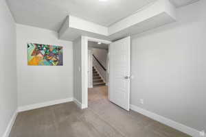 Finished below grade area with a textured ceiling, carpet floors, and stairway
