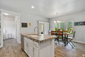 Kitchen with white cabinets, hanging light fixtures, light wood finished floors, a chandelier, and a textured ceiling