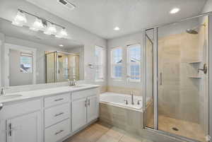 Full bathroom with double vanity, a bath, a shower stall, light tile patterned flooring, and a textured ceiling