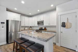 Kitchen with stainless steel appliances, white cabinetry, recessed lighting, light countertops, and a kitchen breakfast bar
