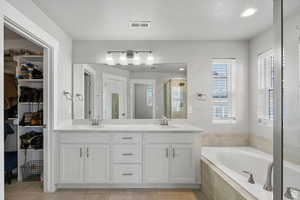 Bathroom featuring a bath, double vanity, a shower stall, a textured ceiling, and a spacious closet