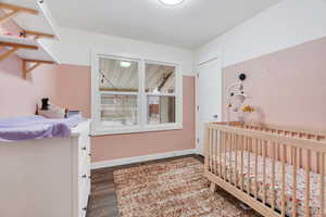 Bedroom with a nursery area and dark wood-style floors