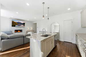 Kitchen with light stone countertops, pendant lighting, open floor plan, dark wood-style flooring, and an island with sink