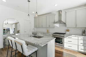 Kitchen with pendant lighting, stainless steel range with gas cooktop, wall chimney range hood, light stone countertops, and recessed lighting