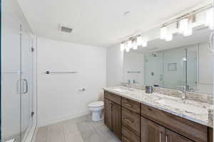 Full bathroom featuring double vanity, a shower stall, a textured ceiling, and light tile patterned floors