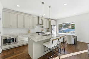 Kitchen featuring light stone countertops, wall chimney exhaust hood, a breakfast bar, pendant lighting, and backsplash