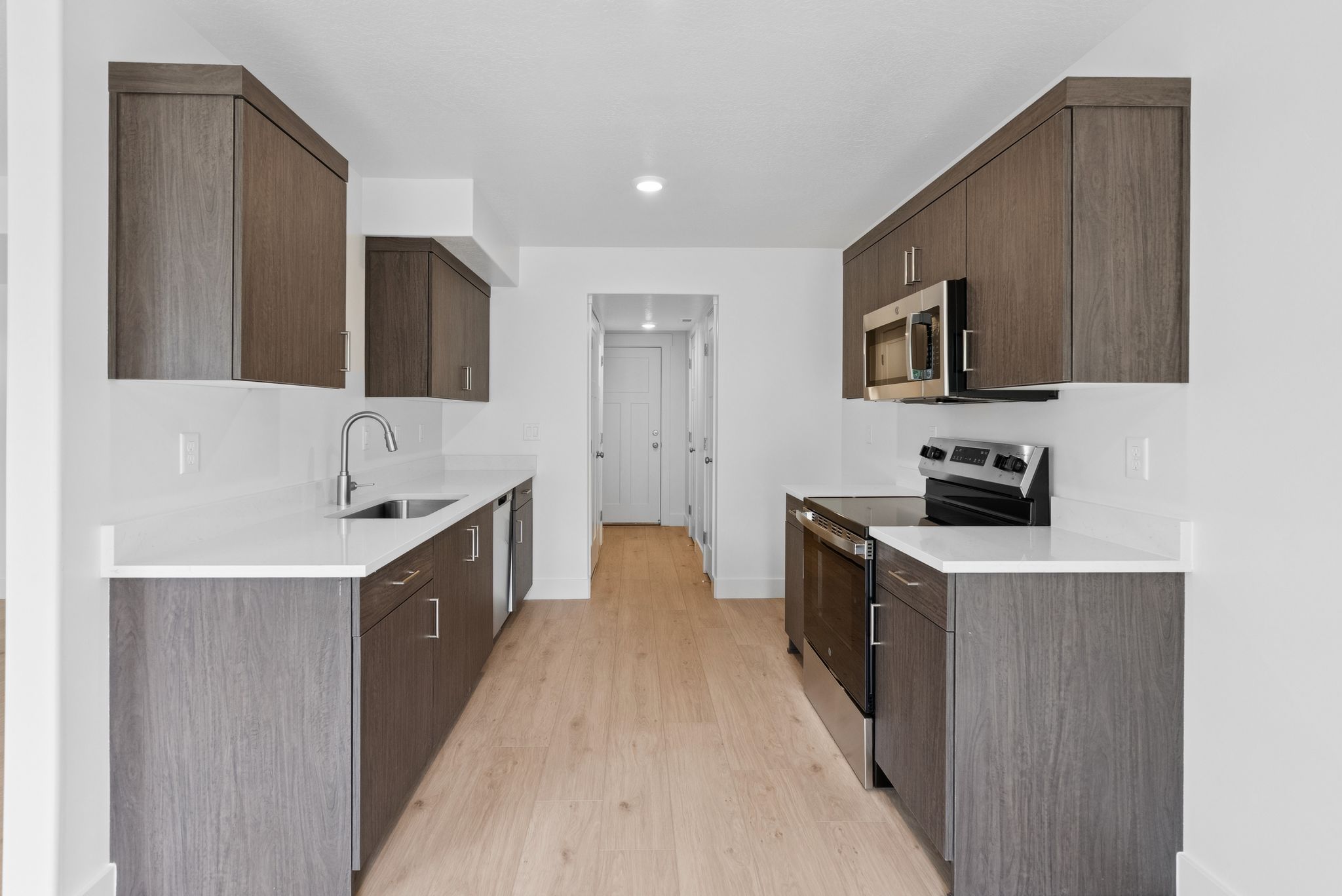 Kitchen featuring stainless steel appliances, dark brown cabinets, modern cabinets, and light wood-type flooring