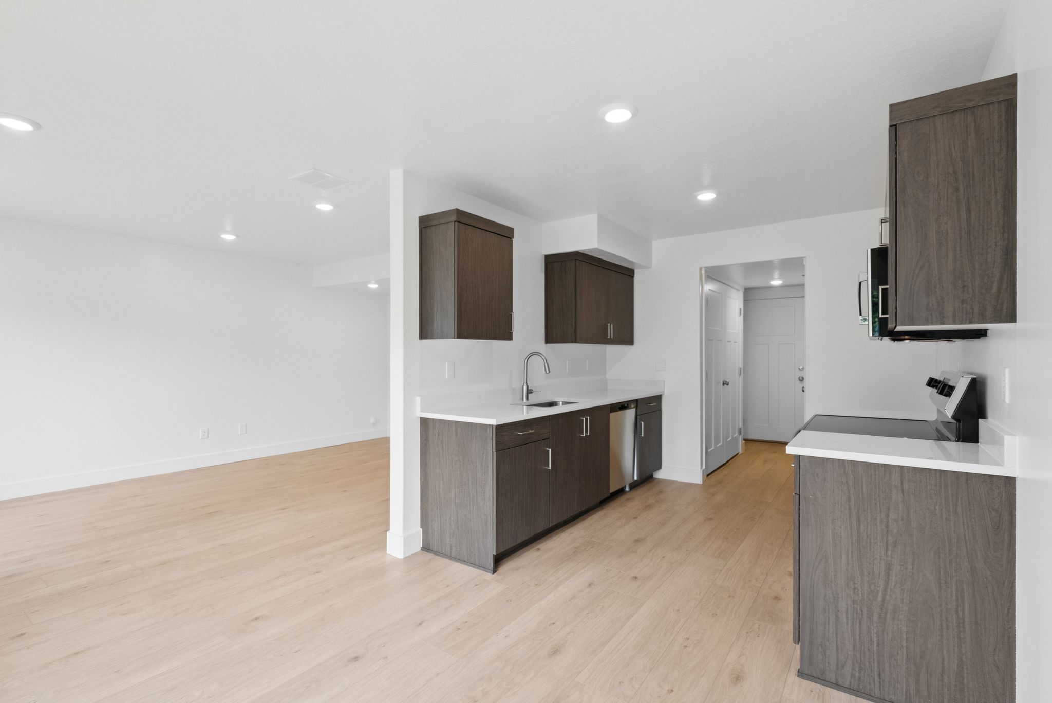 Kitchen with dark brown cabinetry, electric range, light wood-style floors, light stone countertops, and modern cabinets