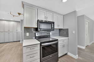 Kitchen featuring electric range, decorative backsplash, light stone counters, light wood finished floors, and recessed lighting