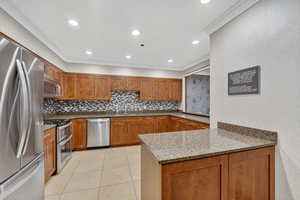 Kitchen featuring light stone countertops, stainless steel appliances, brown cabinets, recessed lighting, and a peninsula