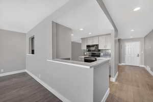 Kitchen with stainless steel range with electric stovetop, backsplash, black microwave, light wood-style floors, and recessed lighting
