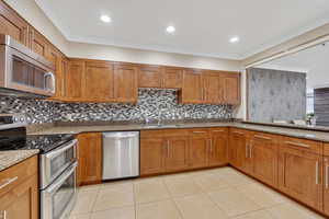 Kitchen featuring stainless steel appliances, wood finish cabinets, light stone countertops, recessed lighting, and ornamental molding