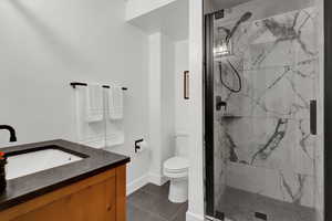 Full bath with vanity, a marble finish shower, and dark tile patterned flooring