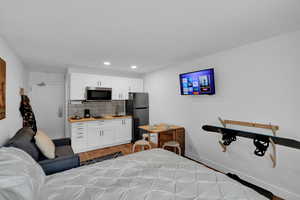 Bedroom featuring freestanding refrigerator, light wood-type flooring, and recessed lighting
