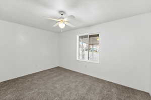 Spare room featuring a textured ceiling, carpet, and a ceiling fan