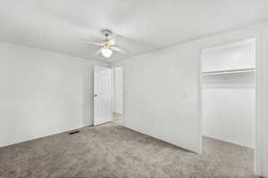 Unfurnished bedroom with a spacious closet, carpet, a textured ceiling, and a ceiling fan