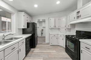 Kitchen featuring black appliances, white cabinetry, light countertops, light wood finished floors, and under cabinet range hood